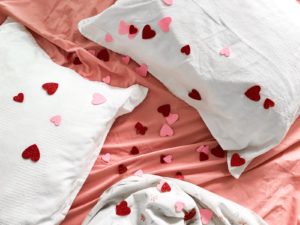 Pillows on a bed with pink sheets and confetti hearts strewn across them