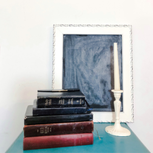 5 Bibles stacked with candle stick next to it black board frame in background