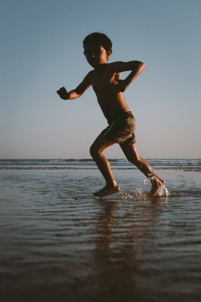 Child runs in sand and ocean water on beach